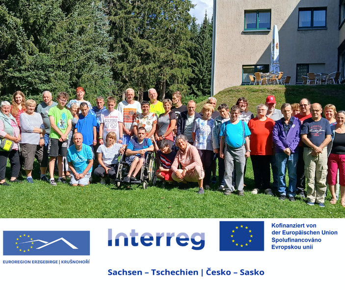 Barrierearme Bildbeschreibung: Gruppenfoto von rund 40 Menschen auf einer Wiese vor einem Gebäude und Bäumen. Im unteren Bildbereich befinden sich die Logos der Euroregion Erzgebirge/Krušnohoří, des Interreg-Programms Sachsen–Tschechien sowie der Hinweis auf die Kofinanzierung durch die Europäische Union.