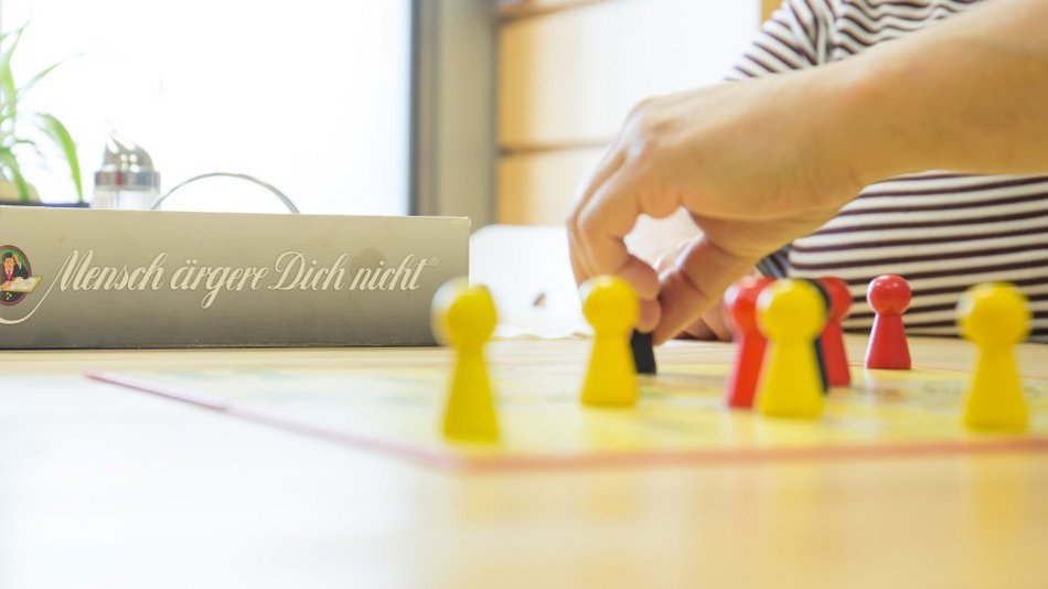 ine Hand setzt konzentriert eine Spielfigur auf dem Spielbrett „Mensch ärgere dich nicht“ – das Brettspiel steht im Mittelpunkt der Szene und sorgt für gesellige Stimmung.