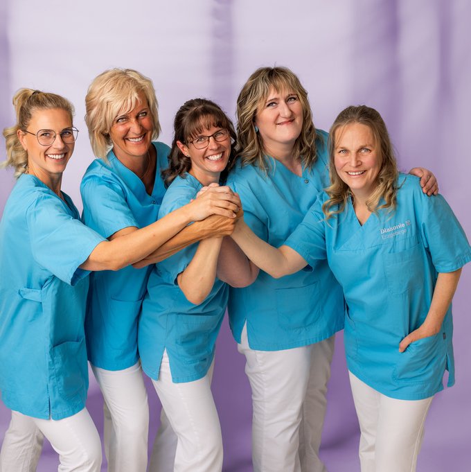 Fünf Pflegekräfte lächeln und halten sich freundschaftlich im Teamfoto