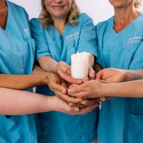 Hände von Pflegekräften halten gemeinsam einen Pokal im Teamfoto