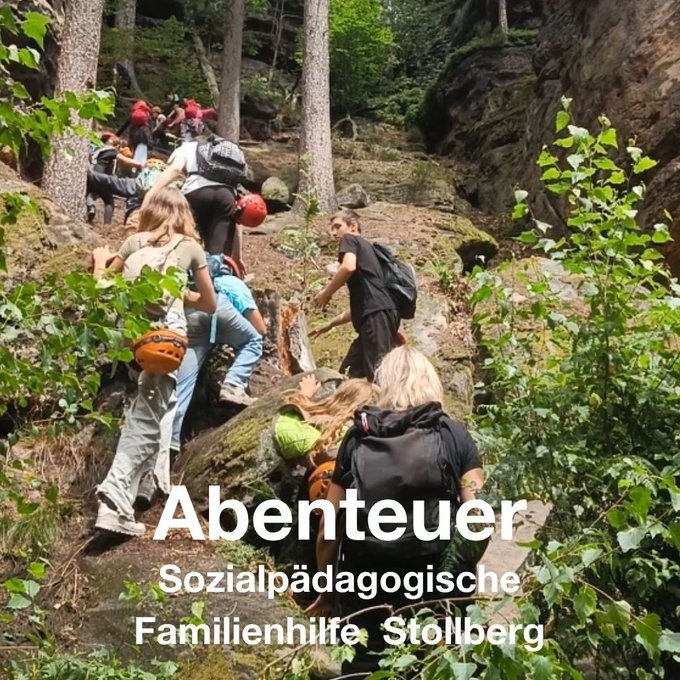 Eine Gruppe Jugendlicher mit Rucksäcken und Kletterhelmen steigt durch eine felsige, bewaldete Schlucht. Im Bild steht der Schriftzug „Abenteuer – Sozialpädagogische Familienhilfe Stollberg“.