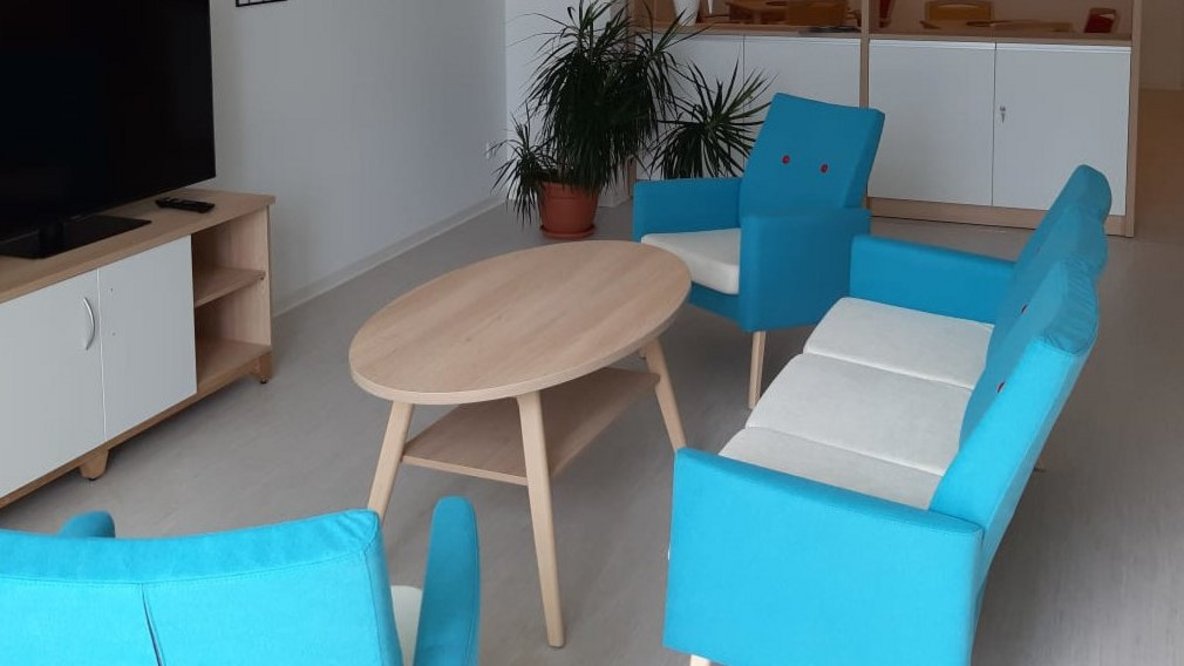 Heller Aufenthaltsraum mit blauen Sesseln und Holztisch