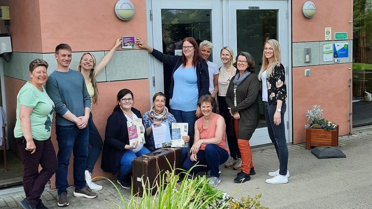 Mitarbeitende der Kita zeigen stolz auf die Auszeichnung zum Eltern-Programm "Schatzsuche"