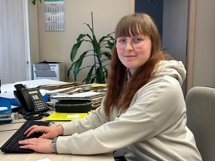 Junge Frau mit Brille arbeitet lächelnd am Schreibtisch im Büro