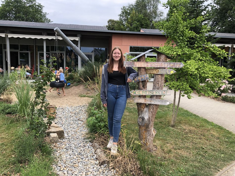 Frau steht lächelnd im Garten vor Gebäude mit Solardach