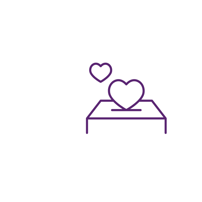 Das Bild zeigt ein einfaches, lilafarbenes Linien-Symbol. Es stellt ein Bett dar, auf dem zwei stilisierte Herzen liegen. Ein größeres Herz befindet sich mittig auf dem Bett, ein kleineres schwebt leicht versetzt darüber. Das Symbol wirkt freundlich und steht sinnbildlich für Pflege, Betreuung oder Fürsorge.