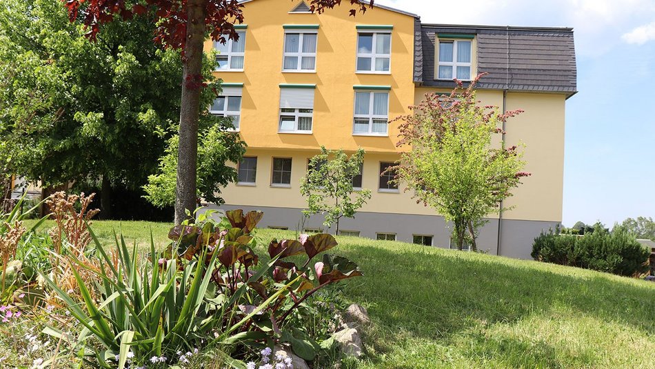 Gelbes Gebäude mit Garten und Bäumen im Vordergrund