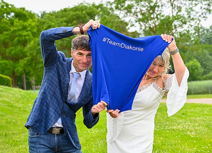 Mann und Frau halten blaues Shirt mit Aufdruck „#TeamDiakonie“ im Freien
