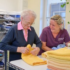 Pflegerin und Senioren legen Wäsche zusammen 