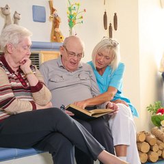 Pflegerin und Senioren lesen ein Buch zusammen 