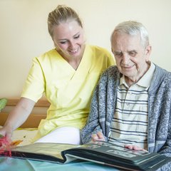 Senior und Pflegerin schauen sich ein Fotoalbum an